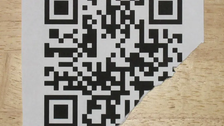 A printed QR code on paper with its lower-right corner torn away, lying on a wooden surface